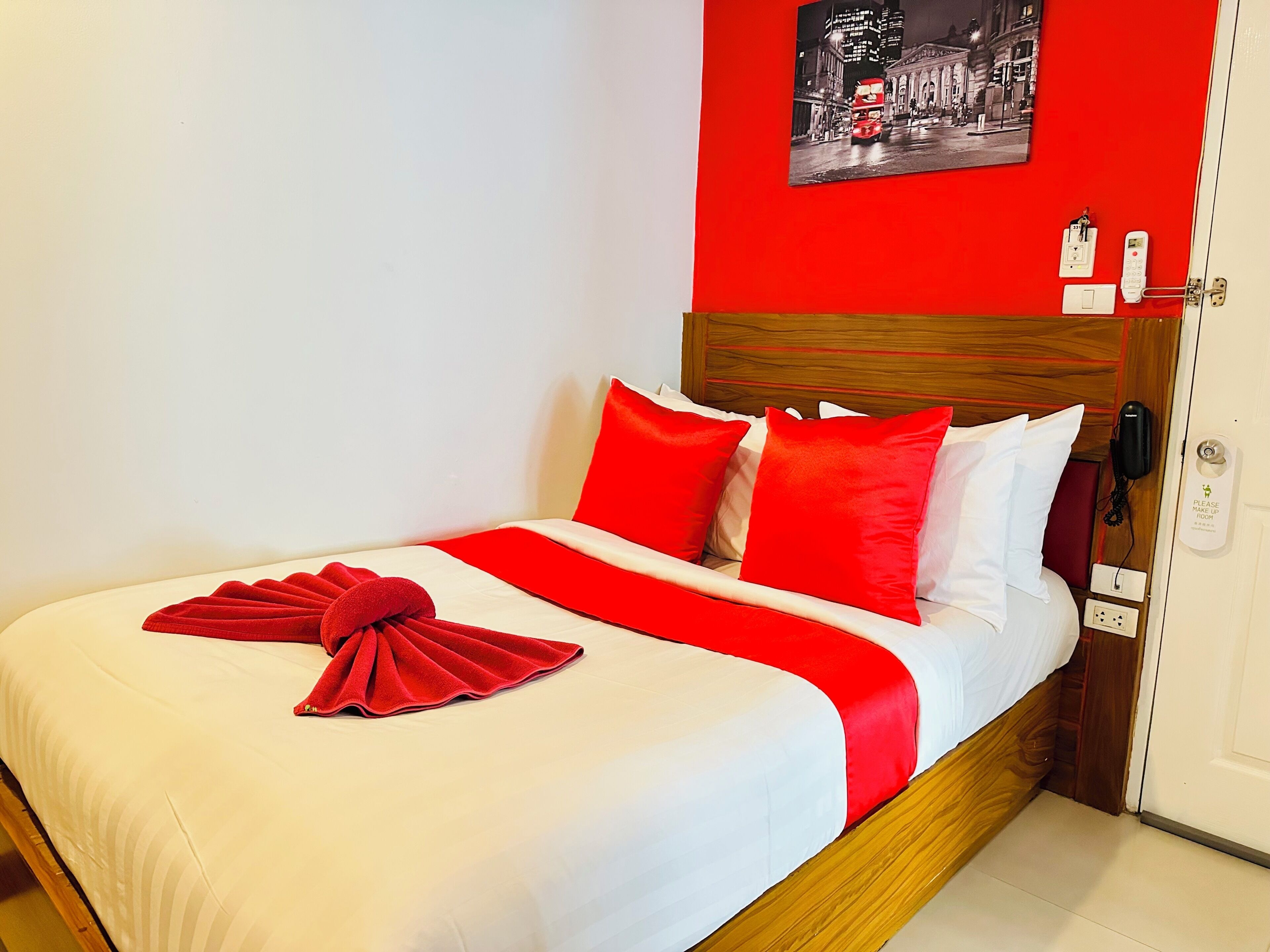 A neatly made bed with red and white bedding, a red towel, and a framed picture on the wall.