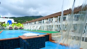 A swimming pool with a waterfall feature, lounge chairs, and a view of a mountainous landscape. - PJ Patong Resortel (Patong)