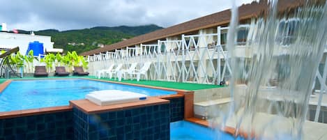 A swimming pool with a waterfall feature, lounge chairs, and a view of a mountainous landscape.