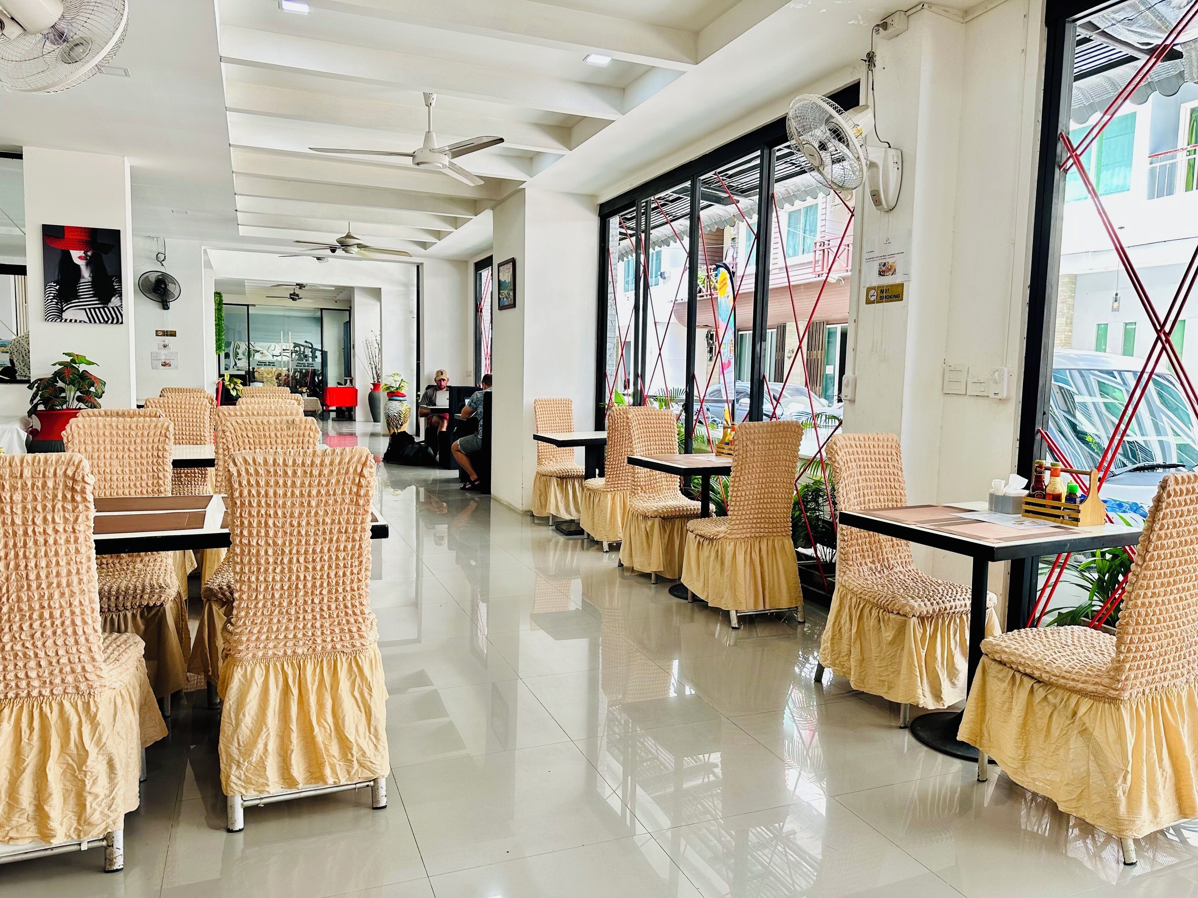 A restaurant with high ceilings, ceiling fans, and large windows offering views of the street.