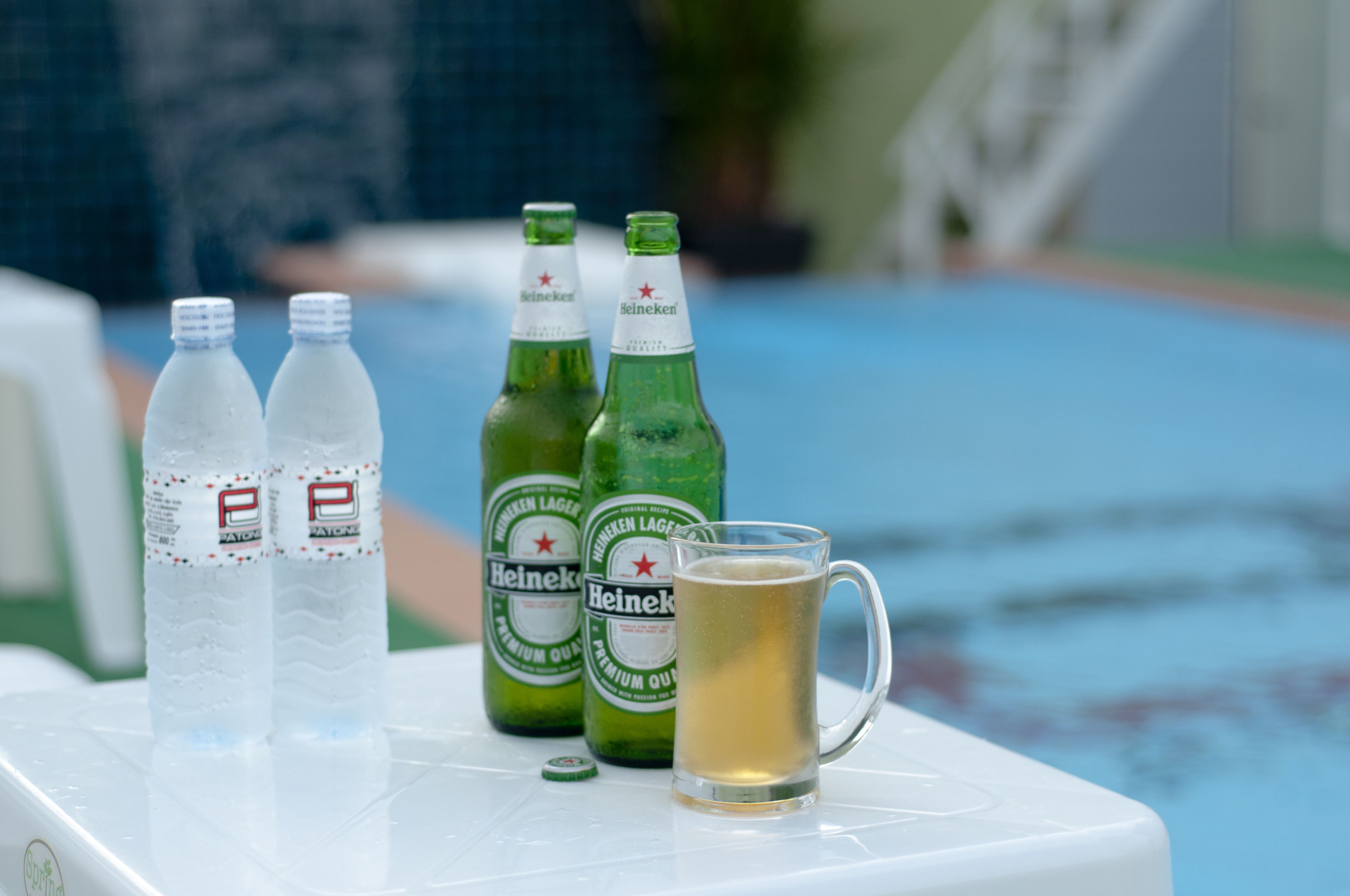 A table with two Heineken bottles and a glass of beer, near a pool.