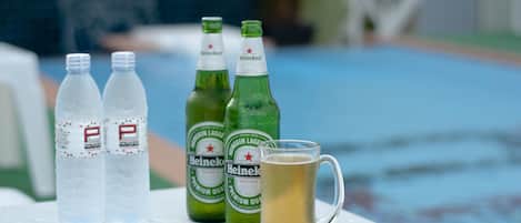 Una mesa con dos botellas de Heineken y una jarra de cerveza, cerca de una piscina.