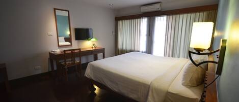 A hotel room with a bed, a desk, a chair, a TV, and a telephone.