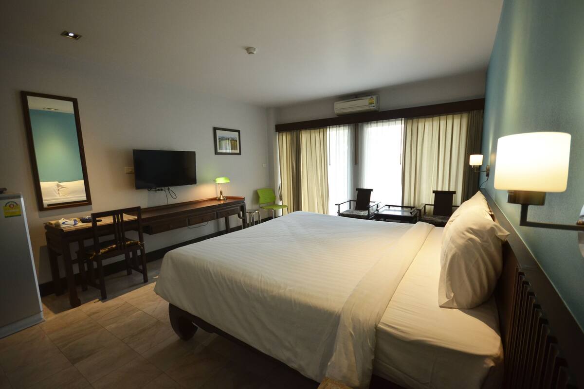 A hotel room with a large bed, a desk with a chair, a television, and a window with curtains.