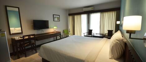 A hotel room with a large bed, a desk with a chair, a television, and a window with curtains.