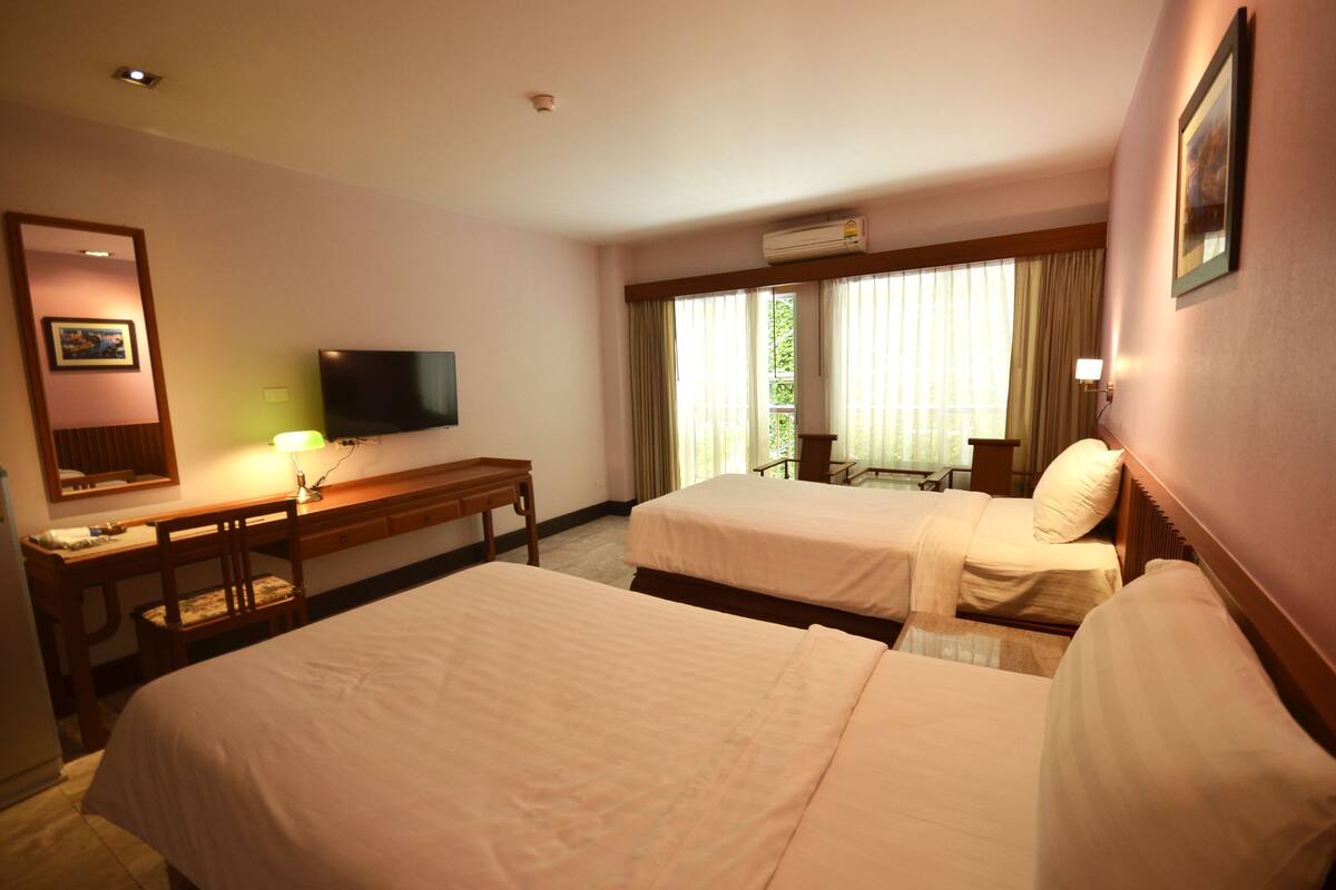 A hotel room with two beds, a desk, a chair, a television, and a window with curtains.