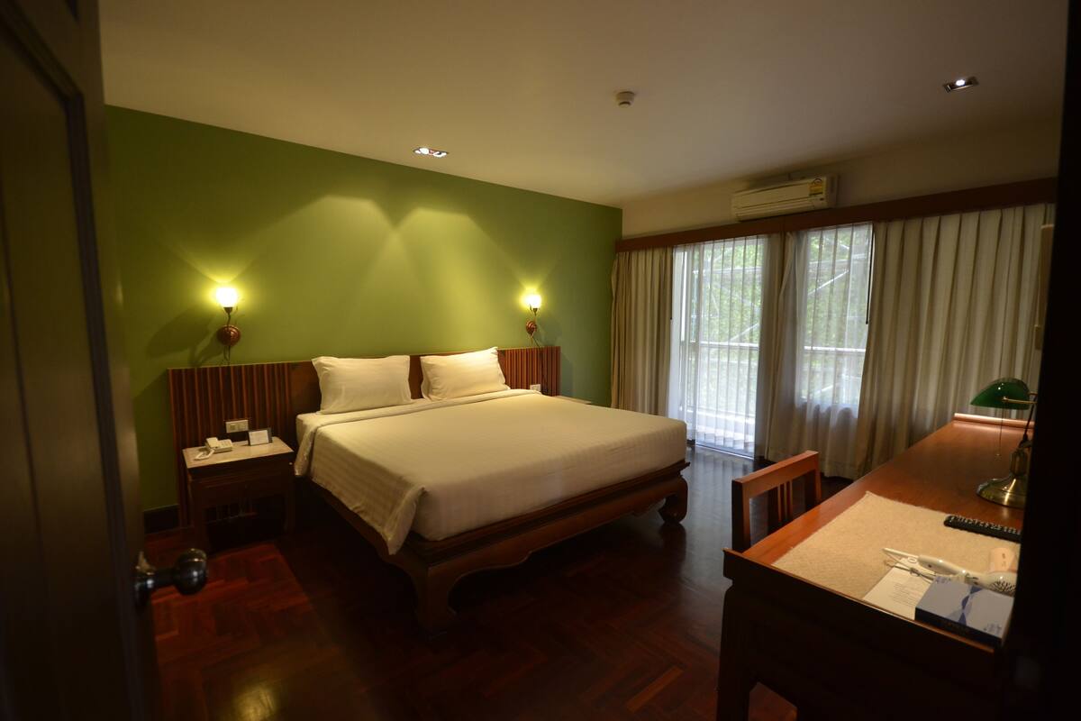 A hotel room with a large bed, two bedside lamps, a desk with a chair, and a window with curtains.