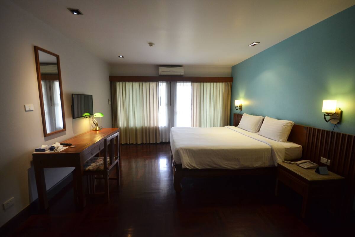 A hotel room with a bed, desk, chair, and a large window with curtains.