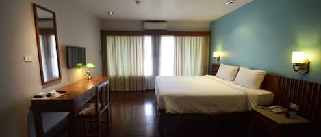 A hotel room with a bed, desk, chair, and a large window with curtains.