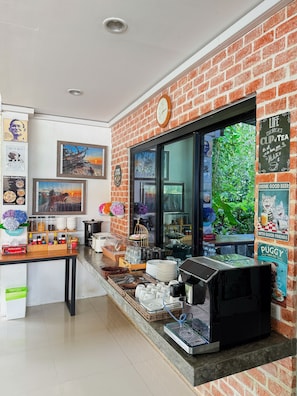 A coffee shop with a brick wall, a coffee machine, and various items on the counter. - Ideo Phuket Hotel (Sa Khu)