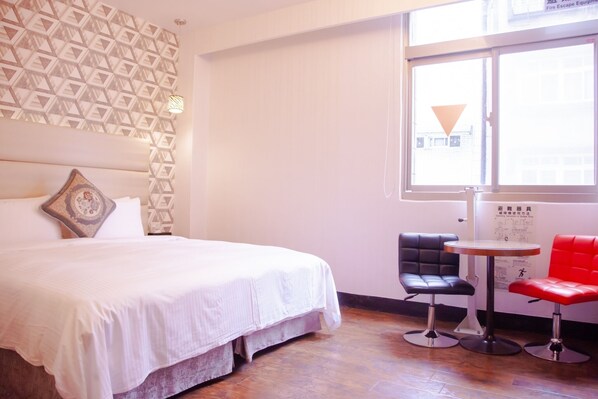 A hotel room with a bed, a patterned wall, a window, and two chairs.