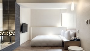 Una habitación de hotel moderna con una cama grande, mesita de noche, lámpara y televisor de pantalla plana.