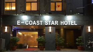 Exterior del Hotel E-Coast Star con alfombra roja, plantas en macetas y señalización iluminada.
