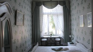 A bedroom with a bed, a window with curtains, a chair, and a small table with a lamp. - Hotel-Pension Fink (Hamburg)