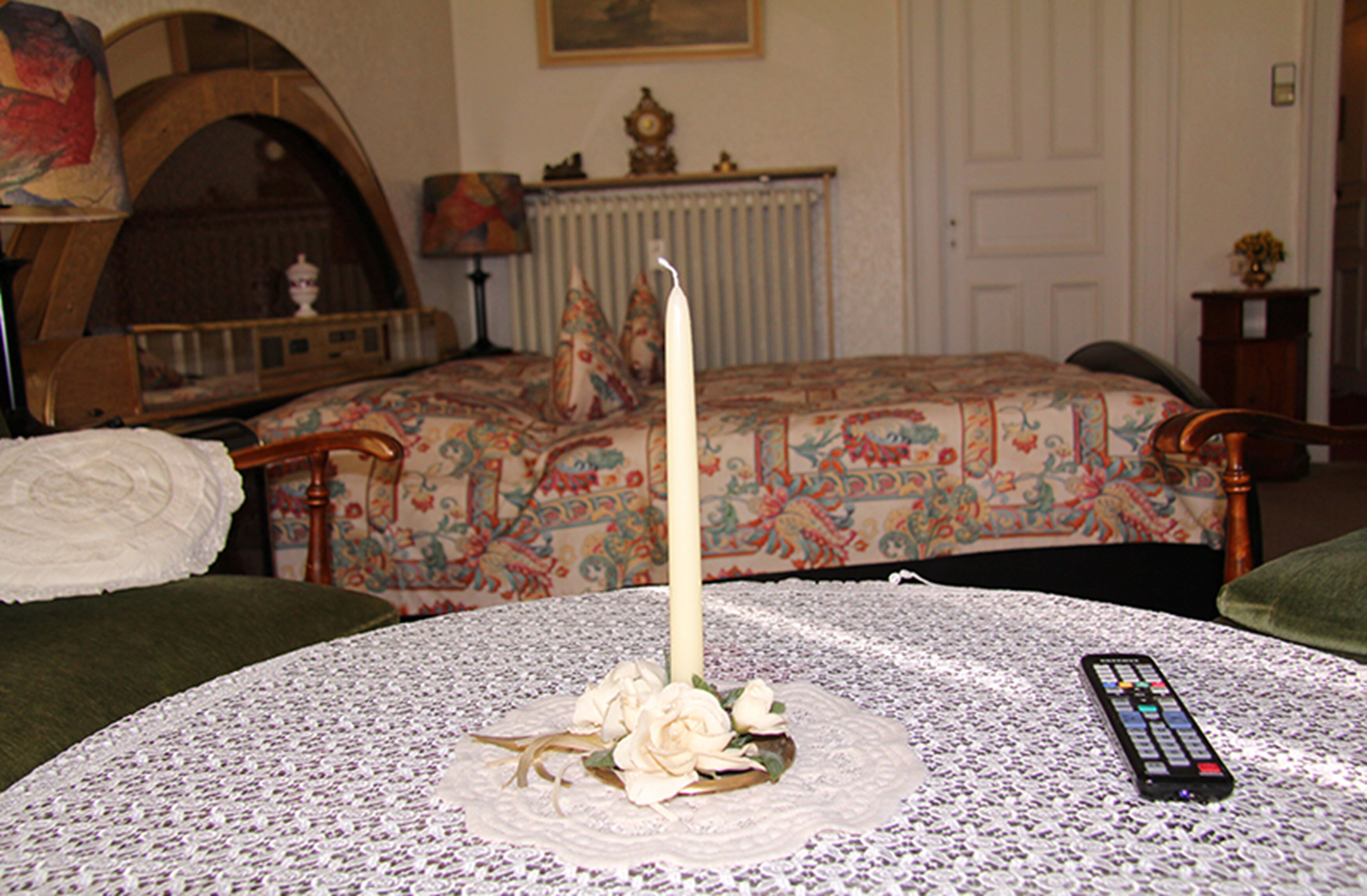 A bedroom with a bed, a round table with a candle and flowers, a remote control, and a fireplace.