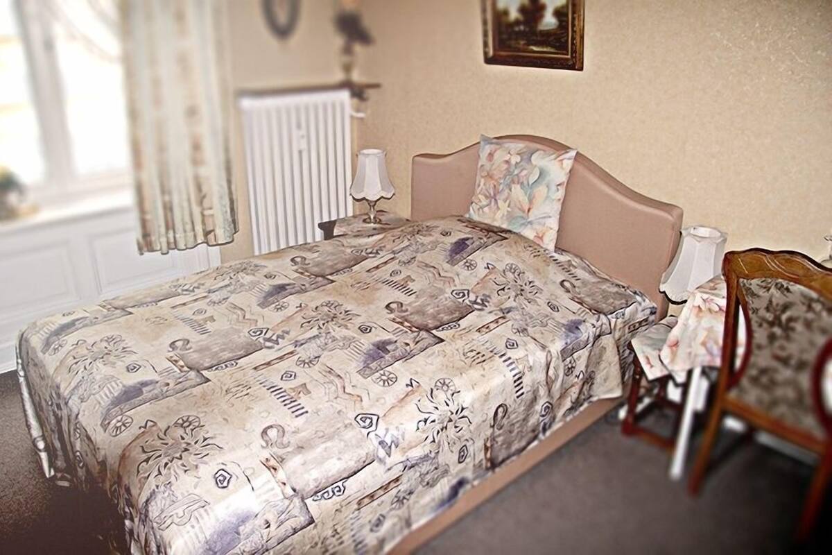 A bedroom with a bed, a bedside table, a chair, and a radiator.