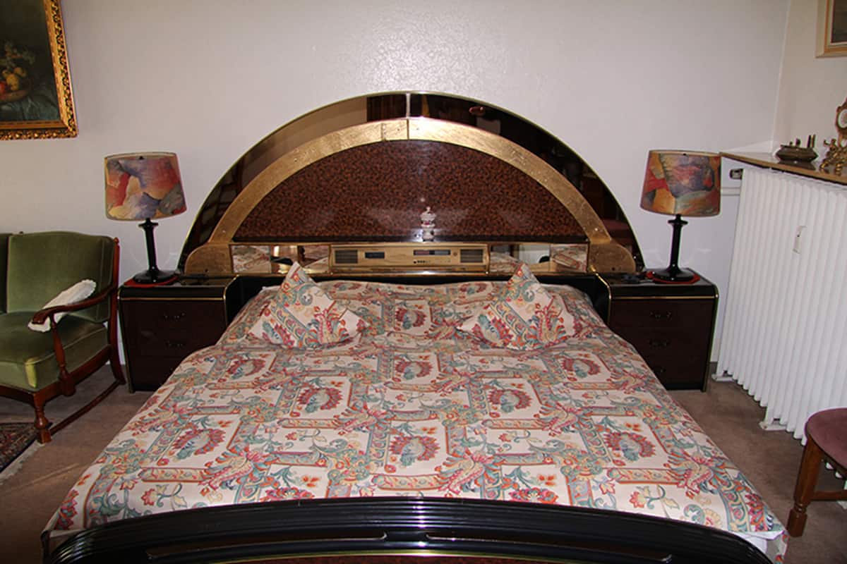 A bedroom with a large bed, two nightstands, a green armchair, and a dresser.