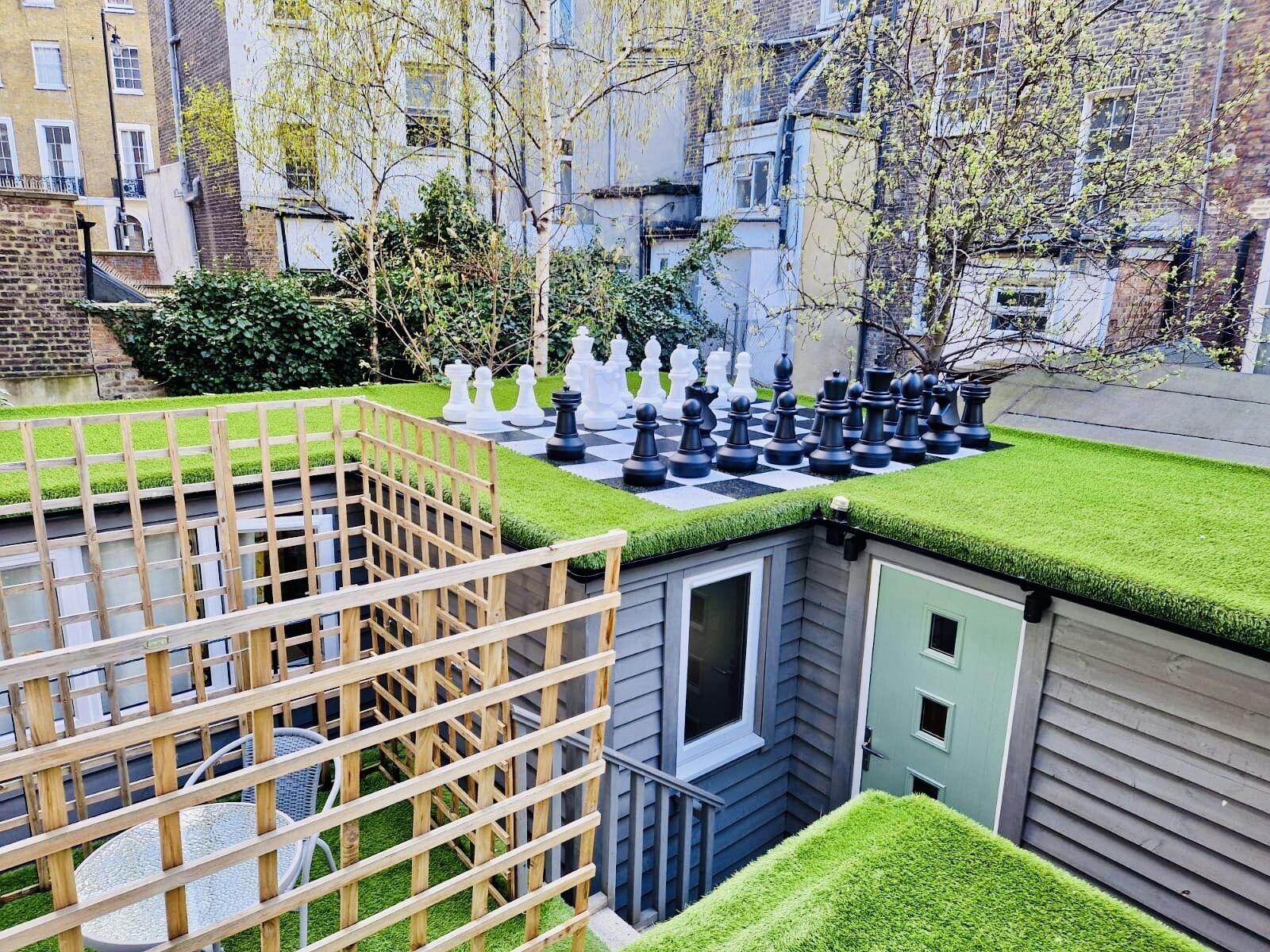 Zona residenziale con una grande scacchiera all'aperto, una recinzione in legno e un piccolo edificio con una finestra.
