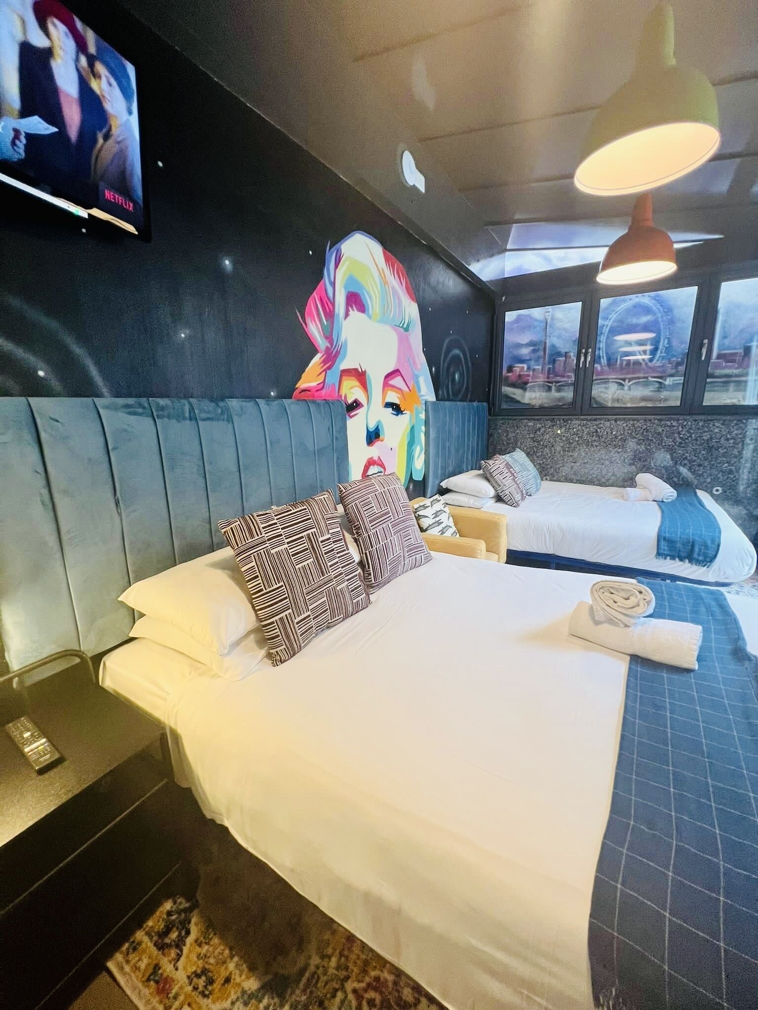 Habitación de hotel con dos camas, un cuadro grande en la pared, un televisor y vista a una noria a través de la ventana.