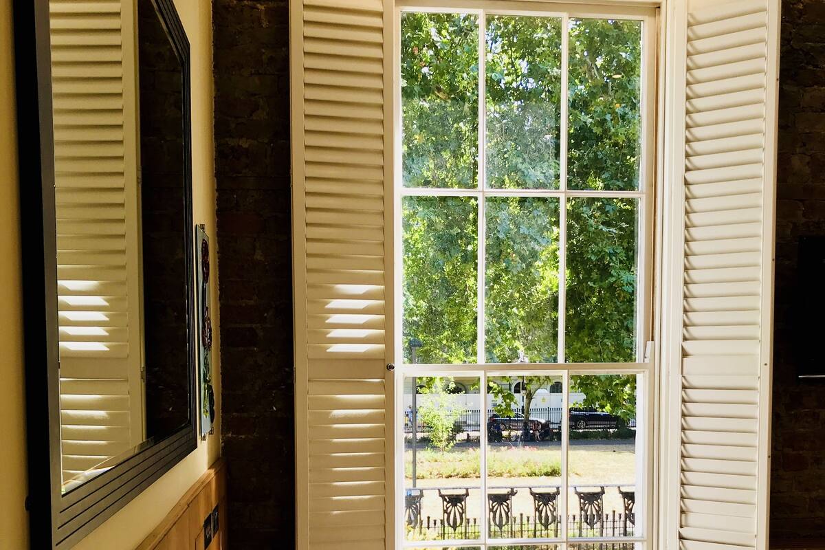 A hotel room with a large window, a bed with white linens, a wooden cabinet, and a mirror on the wall.