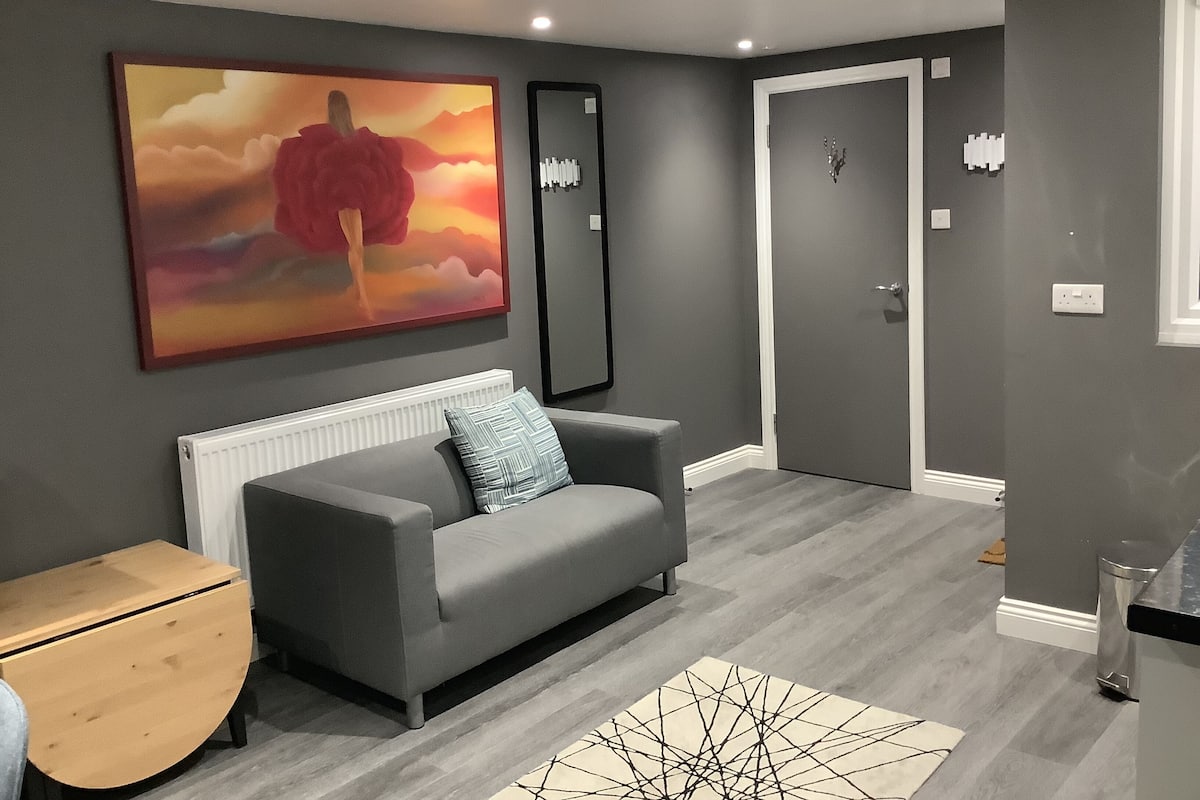 A modern living room with a grey sofa, a wooden side table, a large abstract painting, and a door with a white frame.