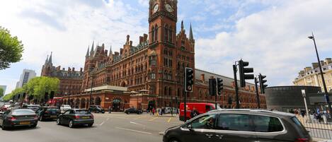A historic building with intricate architecture, a prominent clock tower, and a busy intersection with vehicles and pedestrians.