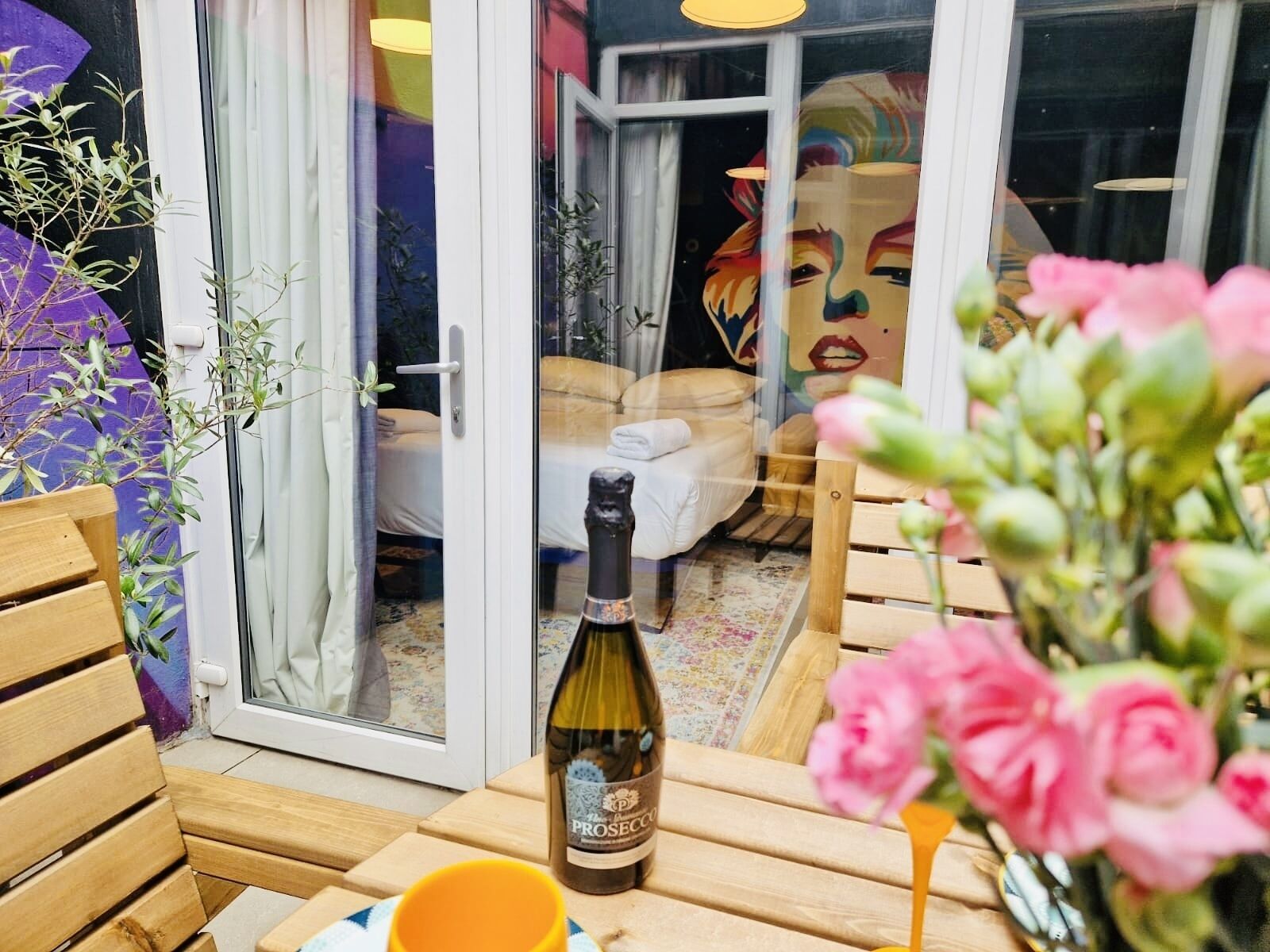 A room with a bed, a bottle of wine, and a vase of flowers.