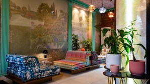 A cozy living room with a sofa, a small table, and a large potted plant. - The Melville Hotel by Rokxy - Kings Cross (London)