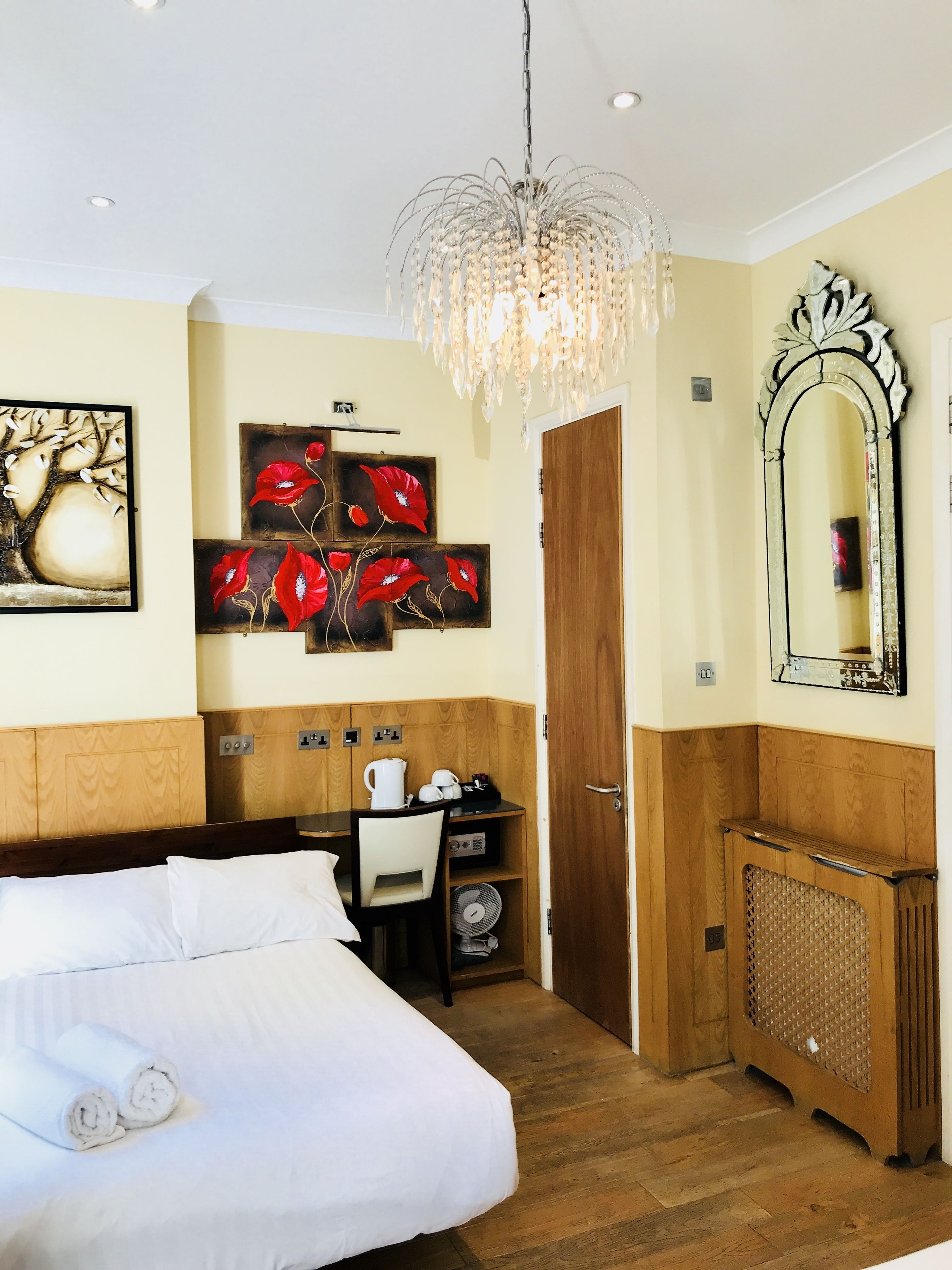 Hotelkamer met een bed, een bureau, een stoel, een radiator, een spiegel en kunstwerken aan de muren.