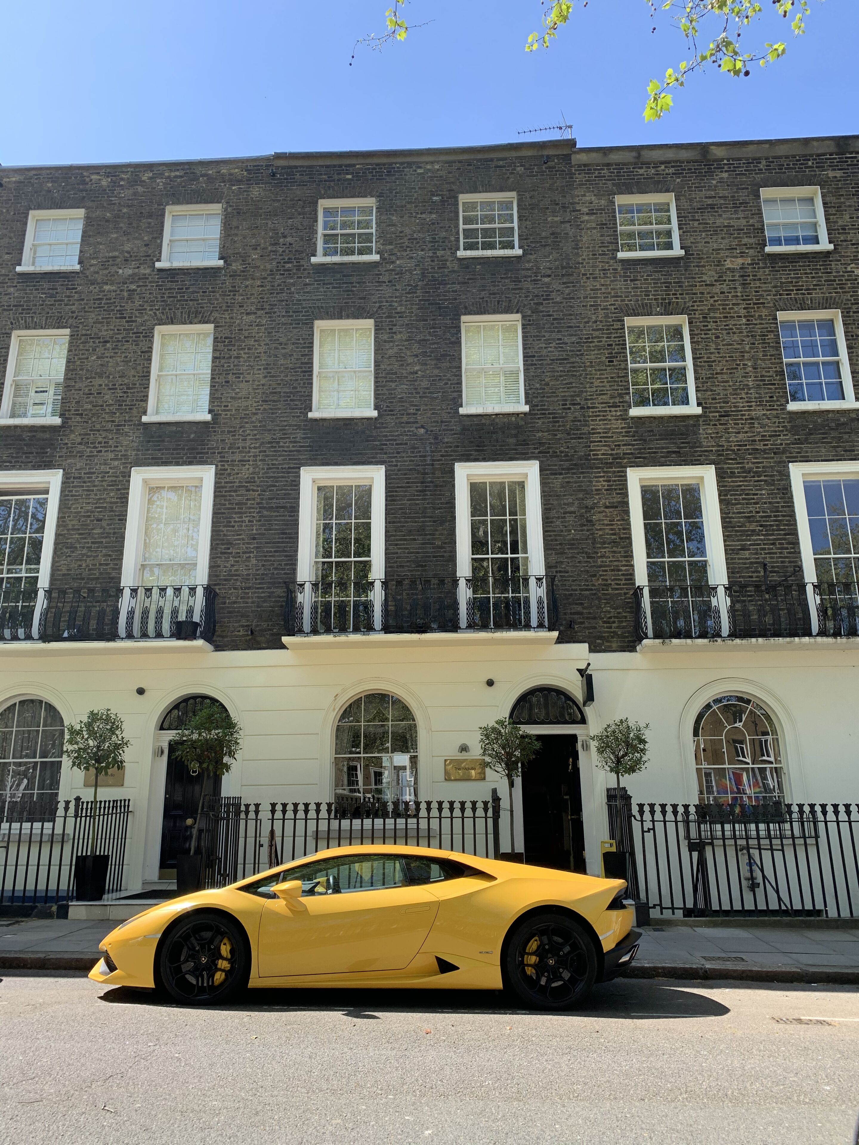 Une voiture de sport jaune est garée devant un bâtiment historique doté de nombreuses fenêtres et d’une façade noire.