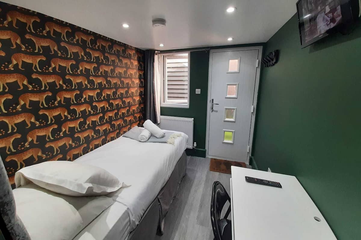 A bedroom with a bed, a desk, a chair, a door, and a window.
