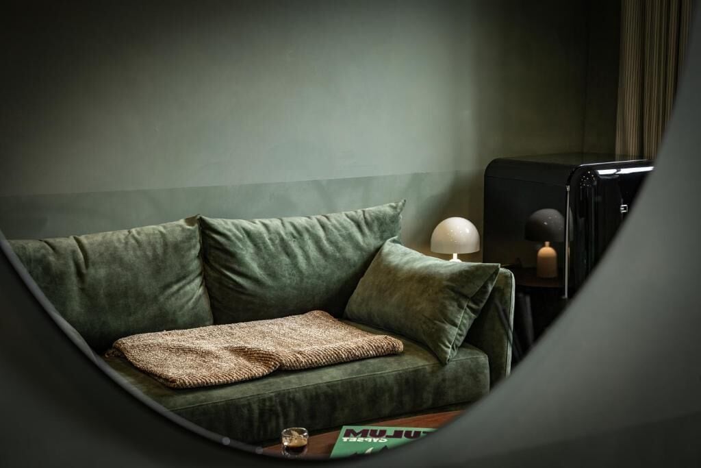 A green sofa with a throw blanket, a lamp, and a small table with a glass.