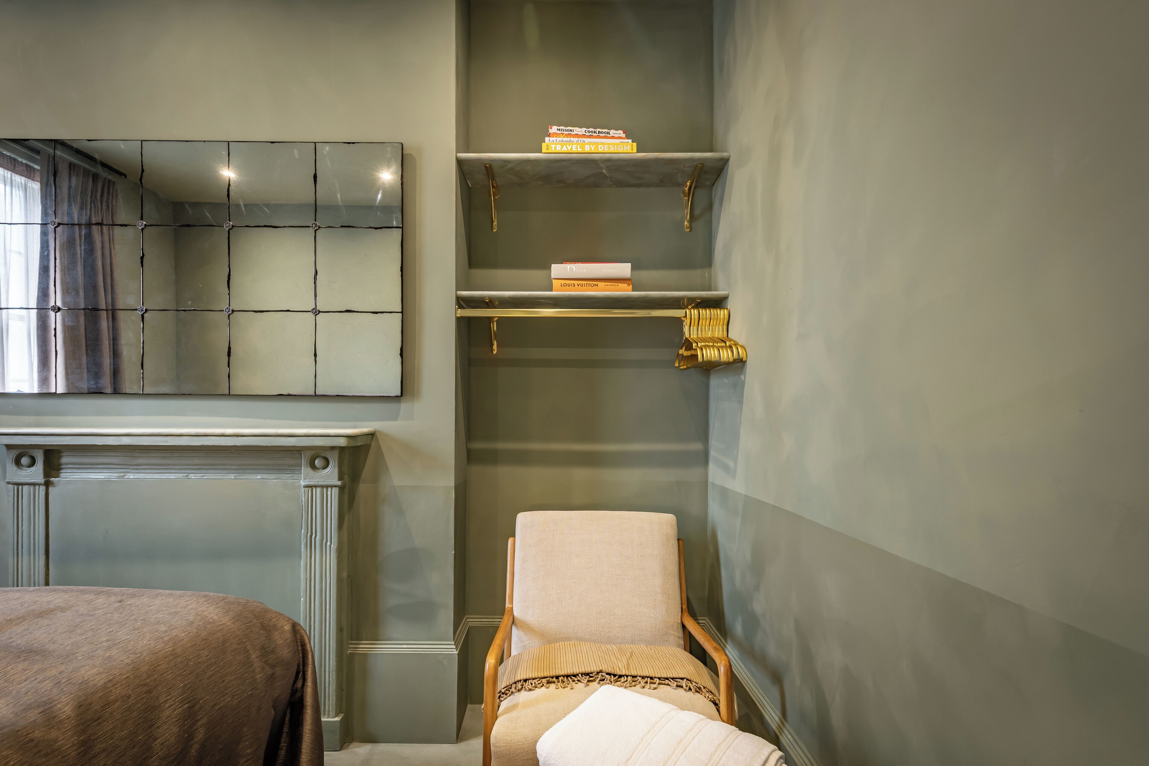 A room with a bed, a chair, a fireplace, and shelves with books.