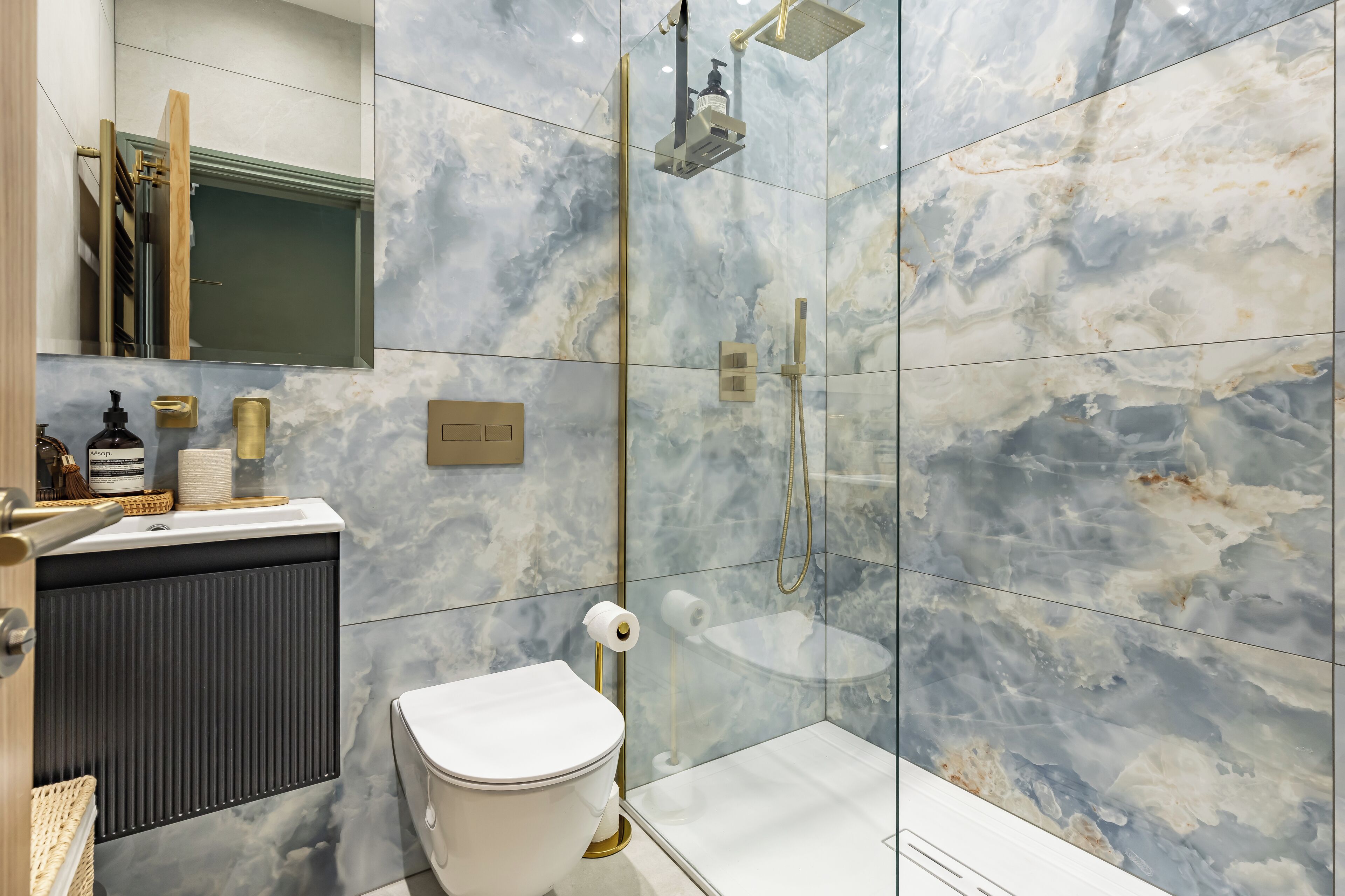 A modern bathroom with a marble backsplash, a toilet, a shower with a glass enclosure, and a vanity with a mirror and towel rack.