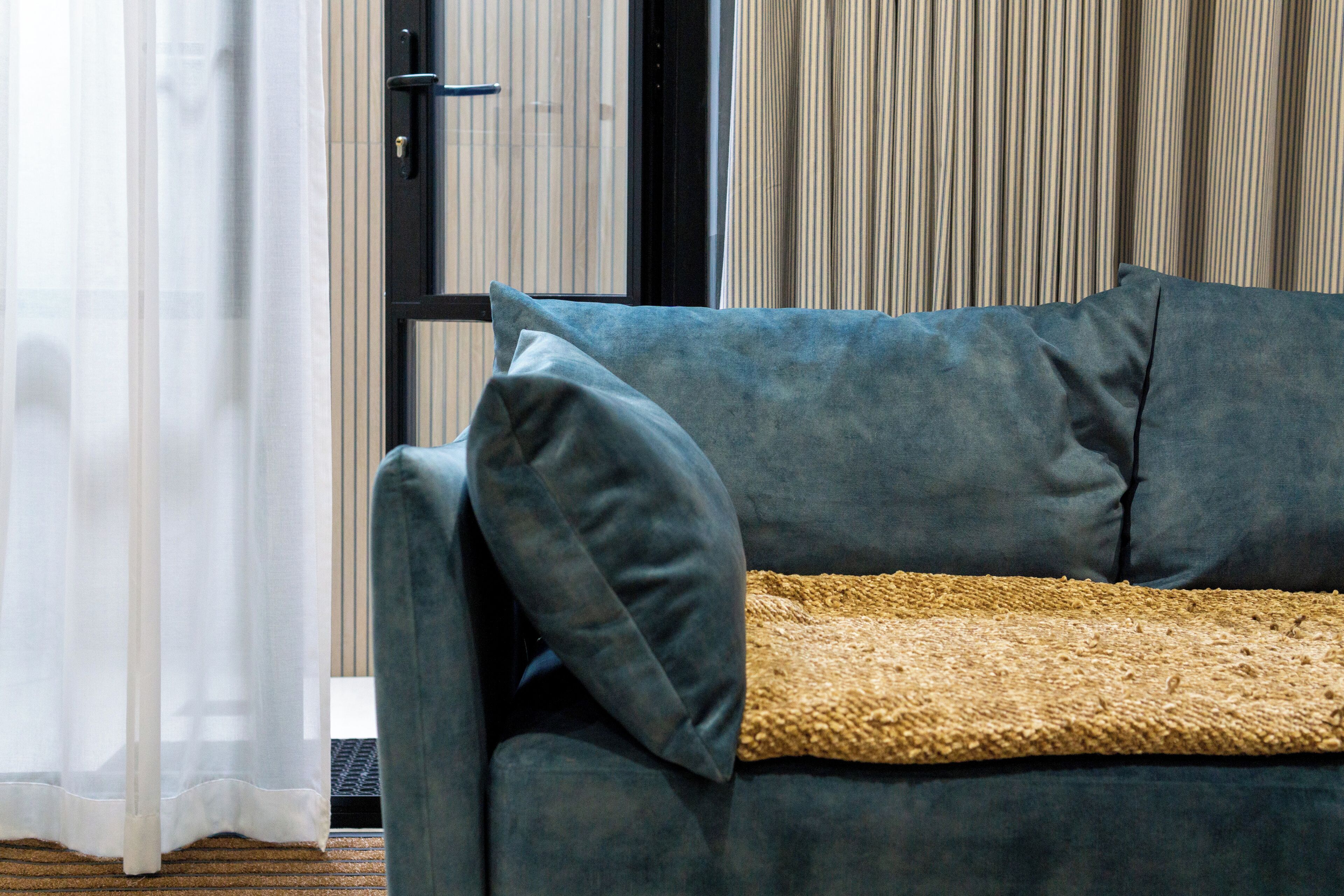 A room with a dark blue sofa, a beige throw blanket, and a sheer white curtain.