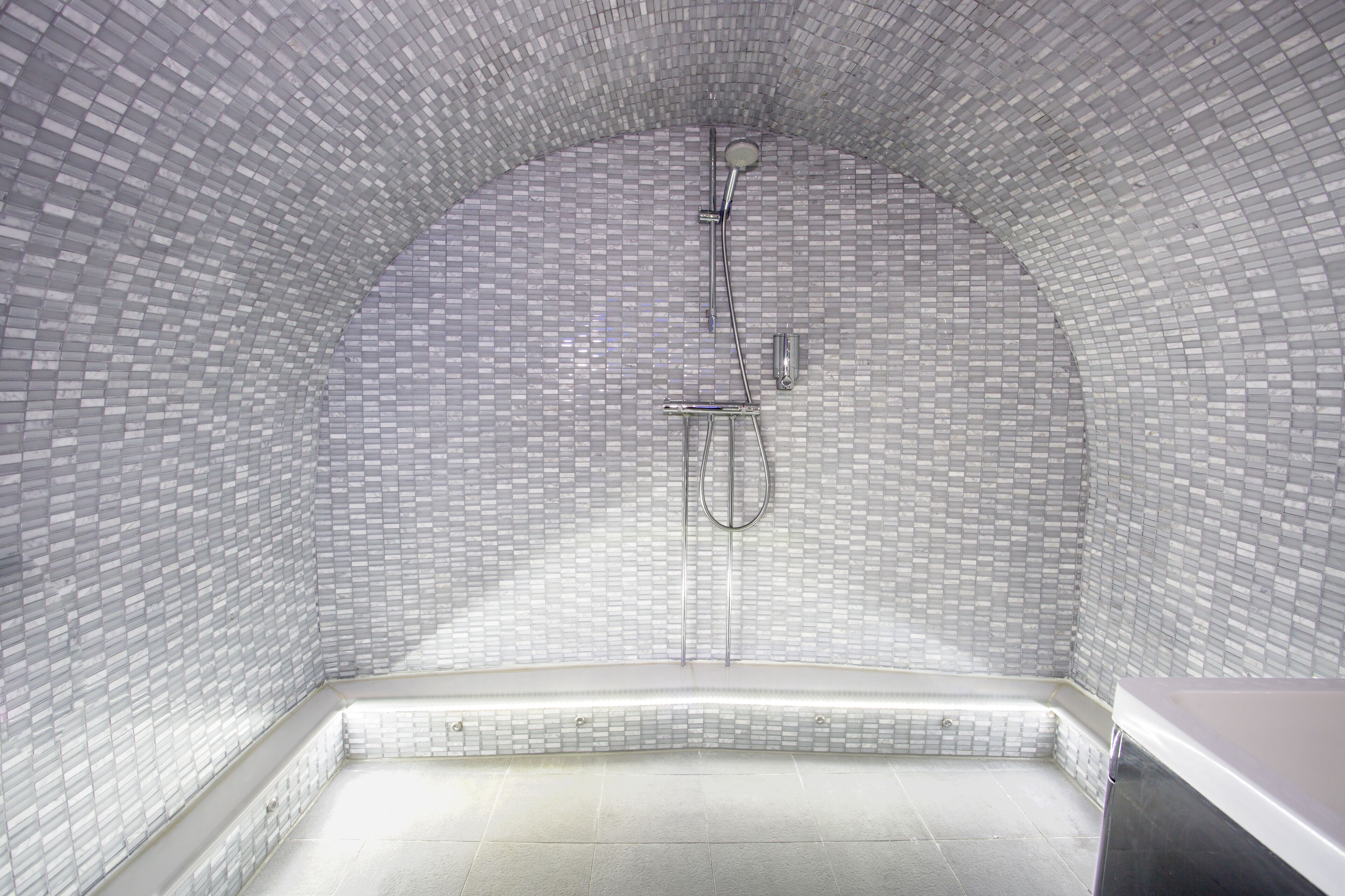 Ein Badezimmer mit Fliesenboden und -wänden, einer Duschkabine mit gewölbter Decke und einer Sitzbank an der Wand.