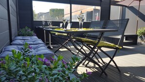 An outdoor seating area with a table and chairs, surrounded by plants and a view of buildings. - Fasthôtel Dunkerque (Grande-Synthe)