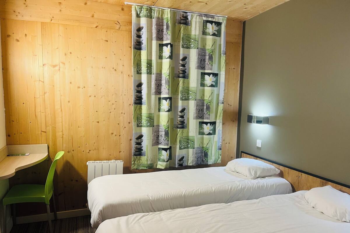 A room with two beds, a desk, a chair, and a curtain with nature-themed prints.