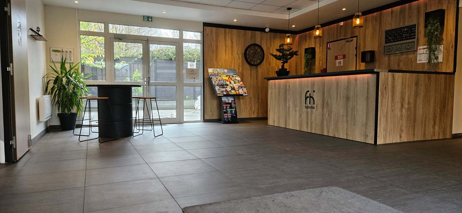 Un área de recepción con mostrador de madera, una planta y un tablón de anuncios.