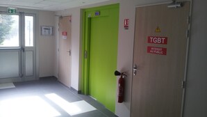 A hallway with a green door, fire extinguisher, and exit signs. - Fasthôtel Dunkerque (Grande-Synthe)