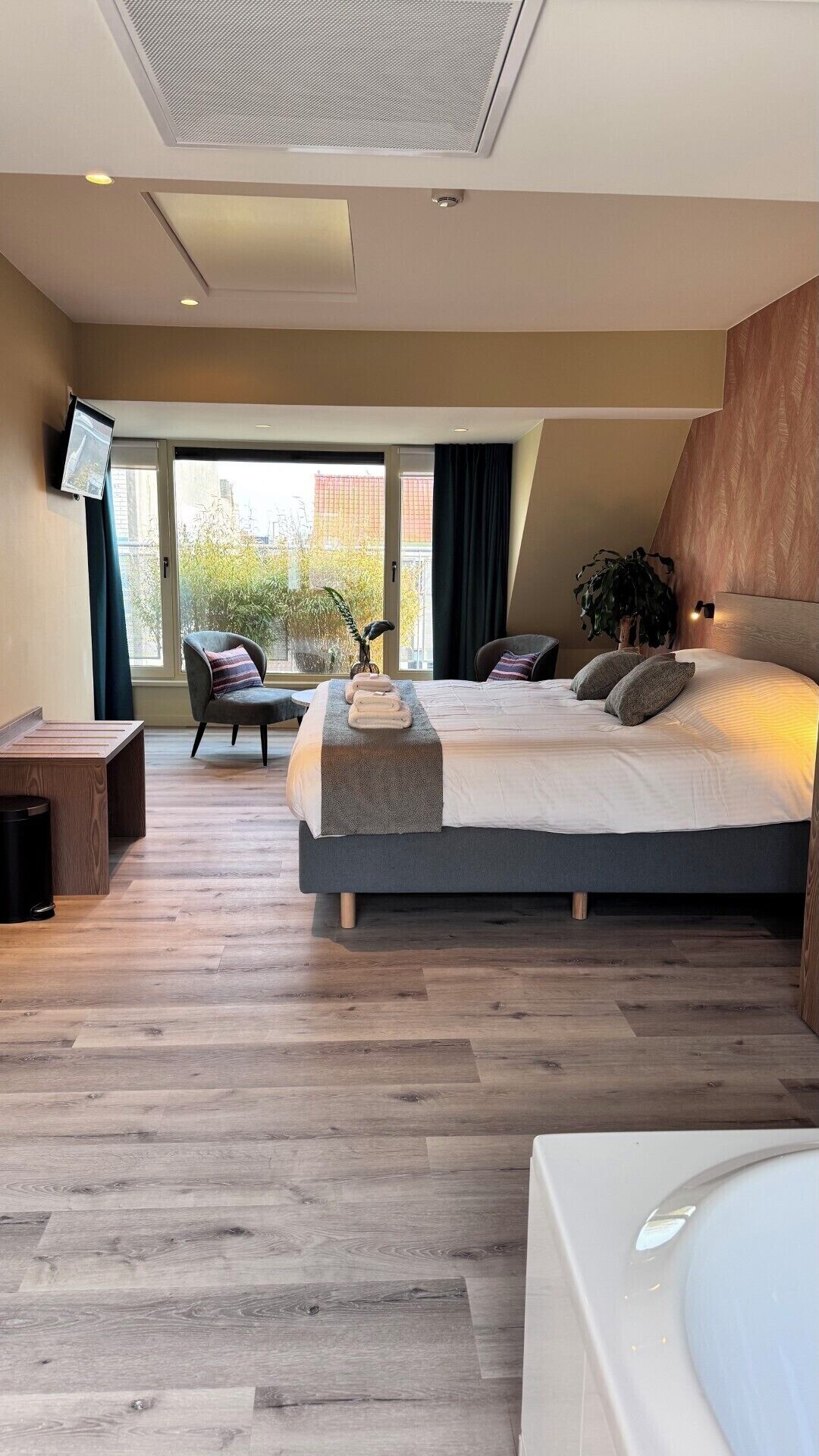 A modern hotel room with a large bed, a seating area with a view, and a television mounted on the wall.