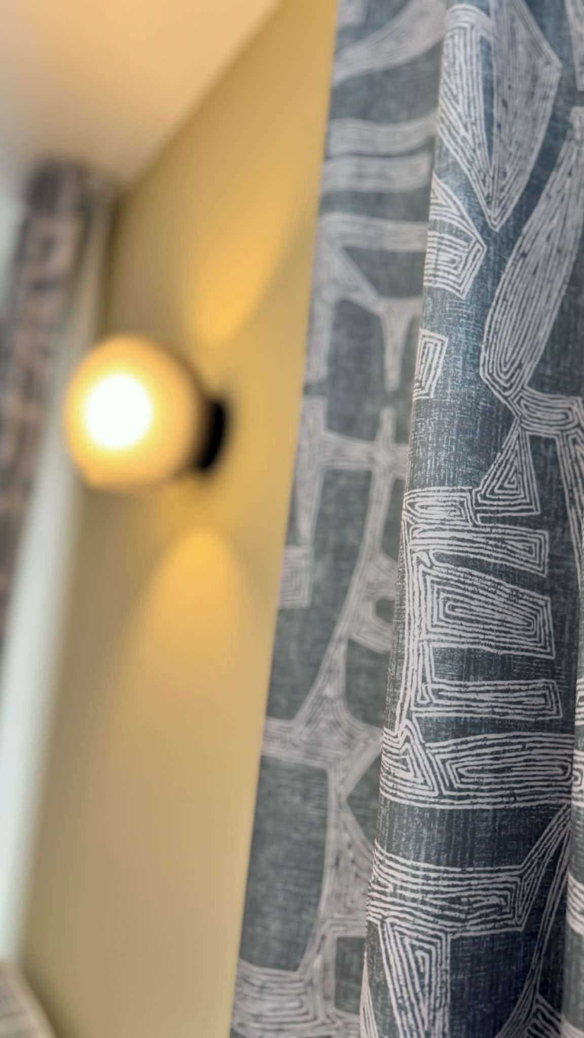 A room with a patterned curtain, a light fixture, and a wall with a textured design.