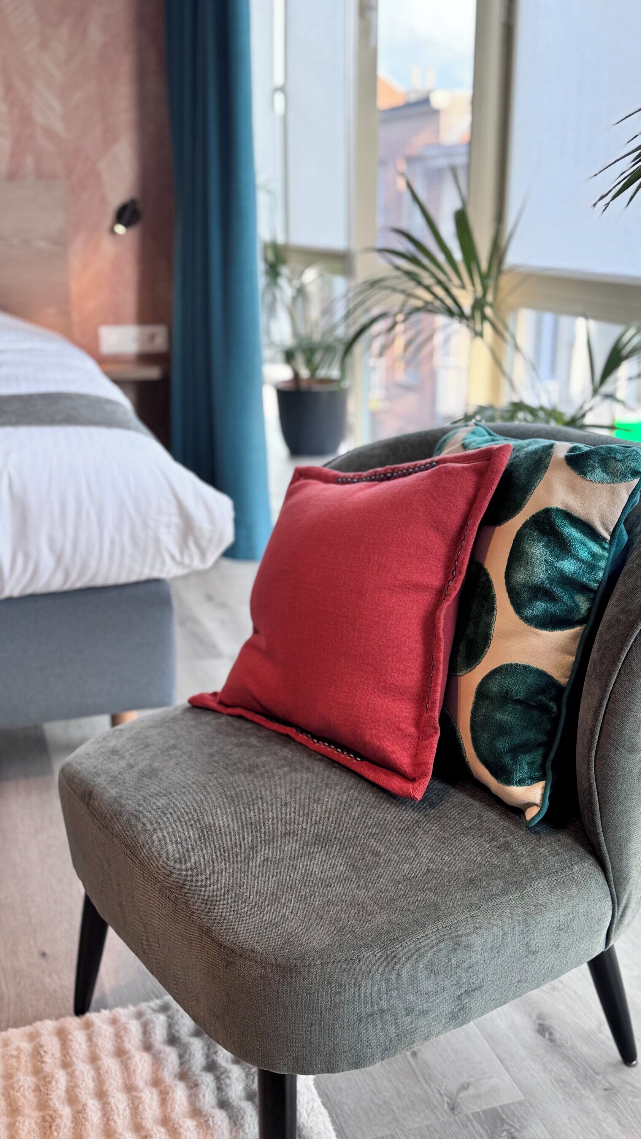 Un salon moderne avec un canapé gris, un coussin rouge et un coussin à motifs verts.