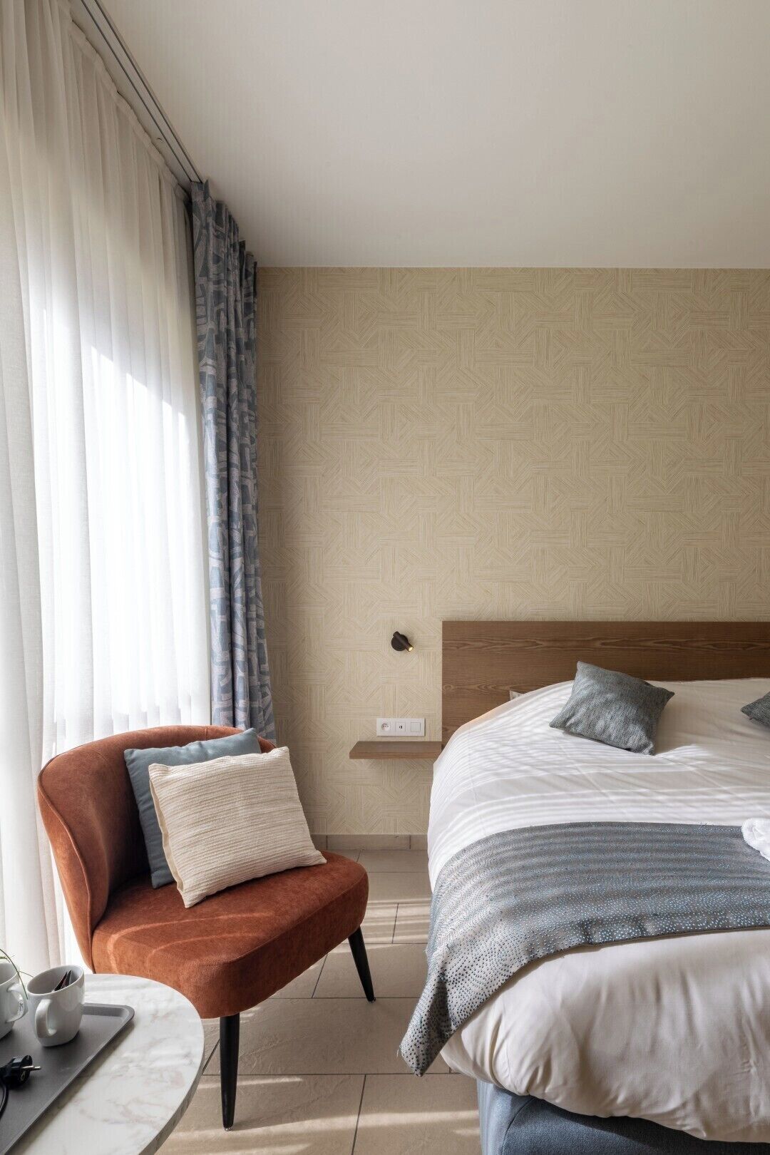 Una habitación de hotel con cama, una silla, una mesa con bandeja y una ventana con cortinas.