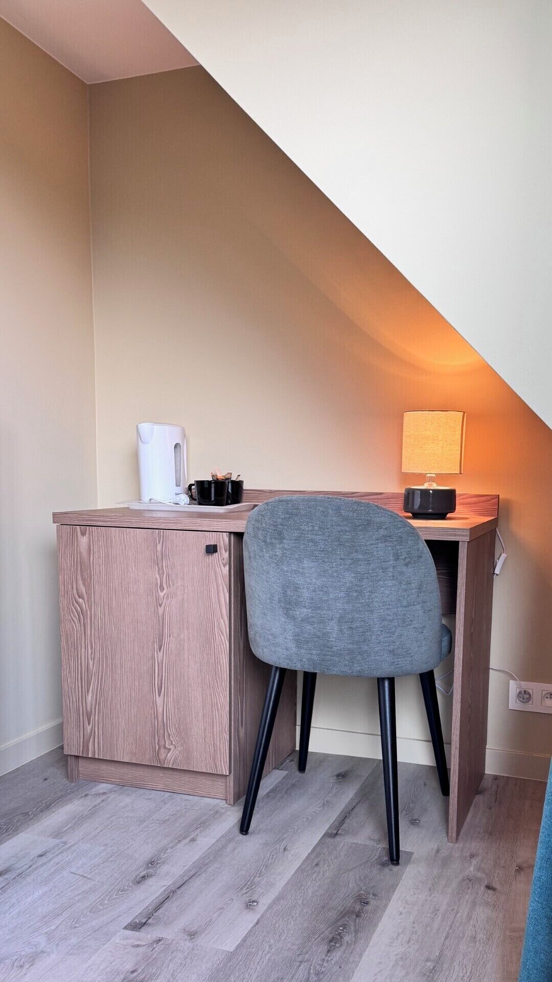 A small, modern room with a desk, a chair, a lamp, and a kettle.