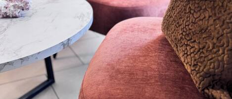 A modern hotel room with a bed, a round coffee table, and a red sofa with a yellow pillow.