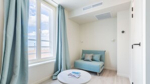 A room with a bed, a small table, a window with curtains, and a view of the sea. - Hotel José (Blankenberge)