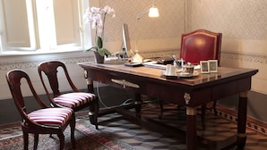 A wooden desk with a computer, lamp, and chair in a room with patterned wallpaper and a window. - Residenza d'Epoca - B&B Santa Caterina (Pisa)