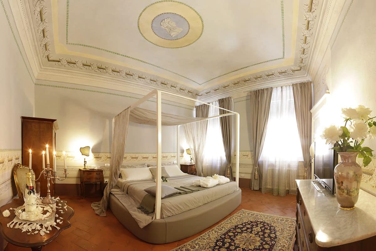 A four-poster bed with a canopy, a vase with flowers, and a chandelier on a nightstand.