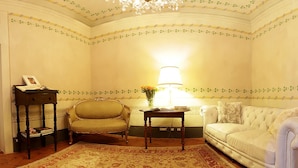 A room with a chandelier, a sofa, a chair, a small table with a lamp, and a patterned rug. - Residenza d'Epoca - B&B Santa Caterina (Pisa)